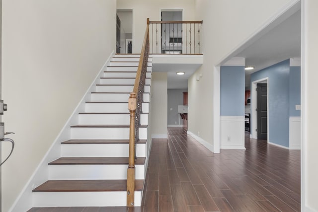 stairway with wood finished floors and a towering ceiling