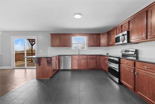 kitchen featuring a breakfast bar, decorative backsplash, appliances with stainless steel finishes, a peninsula, and a sink