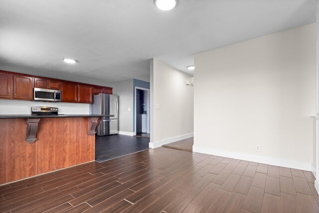 kitchen featuring a kitchen breakfast bar, dark countertops, appliances with stainless steel finishes, baseboards, and dark wood-style flooring