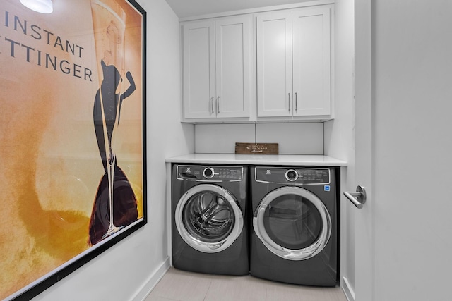 clothes washing area with washing machine and clothes dryer, tile patterned flooring, cabinet space, and baseboards