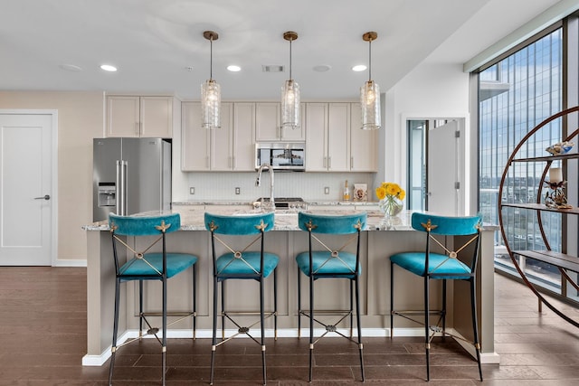 kitchen featuring visible vents, a kitchen island with sink, backsplash, appliances with stainless steel finishes, and dark wood-style flooring