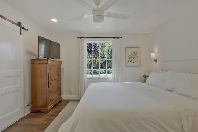 bedroom with wood finished floors, recessed lighting, a barn door, baseboards, and ceiling fan