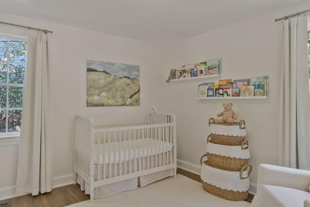 bedroom with visible vents, baseboards, a nursery area, and wood finished floors