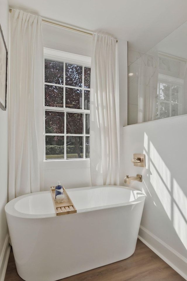 full bath featuring baseboards, a freestanding bath, and wood finished floors