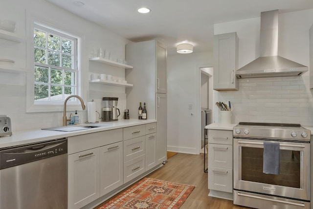 kitchen featuring a sink, light wood-type flooring, appliances with stainless steel finishes, wall chimney exhaust hood, and open shelves