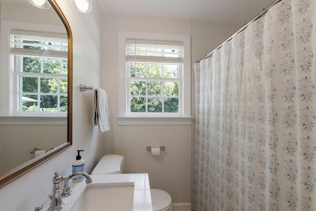 bathroom with a shower with curtain, toilet, a healthy amount of sunlight, and a sink