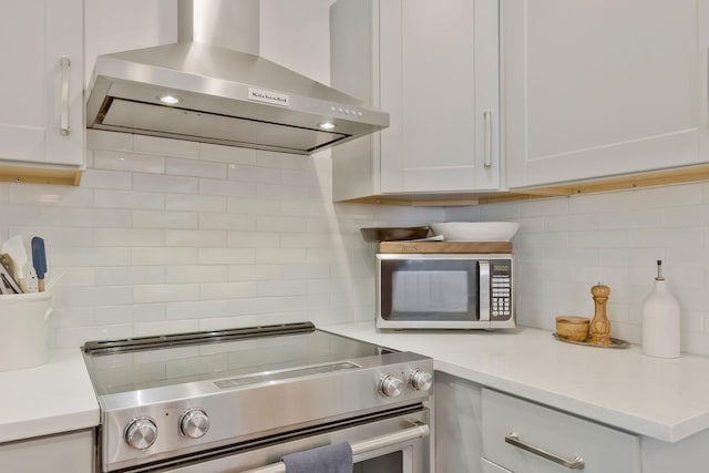 kitchen featuring decorative backsplash, stainless steel appliances, light countertops, and wall chimney range hood