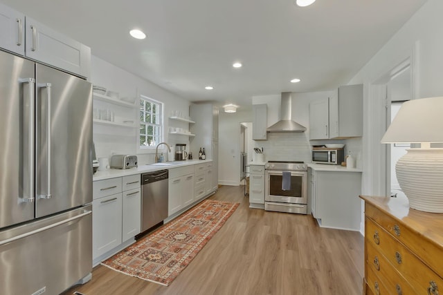 kitchen featuring open shelves, a sink, backsplash, appliances with stainless steel finishes, and wall chimney range hood