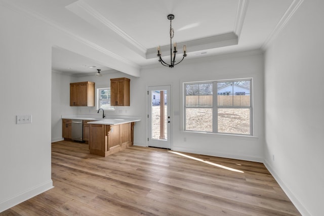 kitchen featuring brown cabinetry, a tray ceiling, light countertops, stainless steel dishwasher, and light wood-type flooring