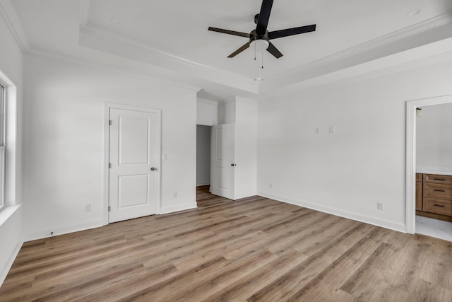 unfurnished bedroom with a tray ceiling, baseboards, light wood-style floors, and crown molding