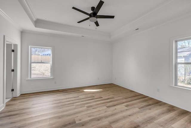 empty room with a tray ceiling, a healthy amount of sunlight, light wood-style flooring, and crown molding