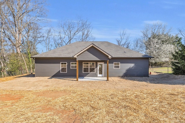 back of property with fence, a shingled roof, and a patio area