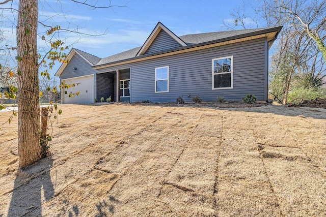 rear view of property featuring an attached garage and a shingled roof