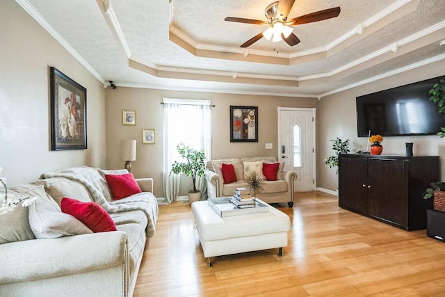 living room featuring a textured ceiling, light wood-type flooring, and a tray ceiling