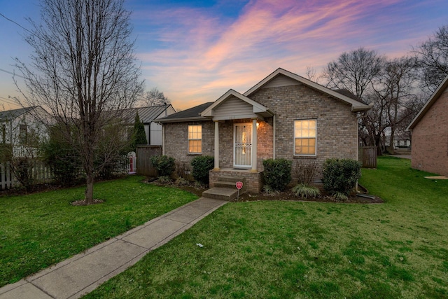 view of front of house with a yard, fence, and brick siding