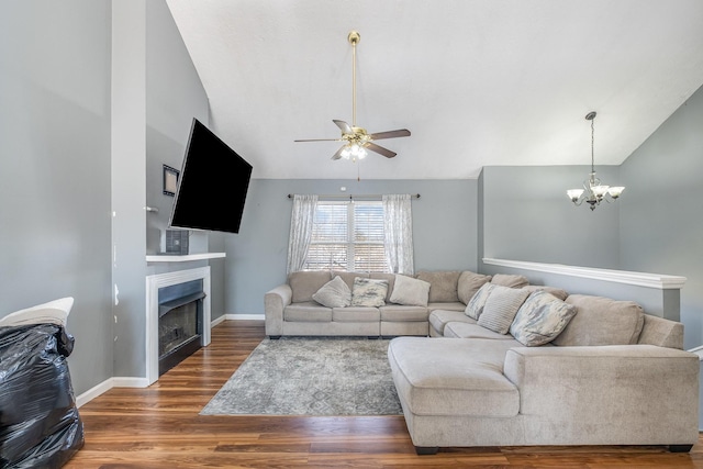 living room featuring ceiling fan with notable chandelier, wood finished floors, a fireplace, baseboards, and vaulted ceiling