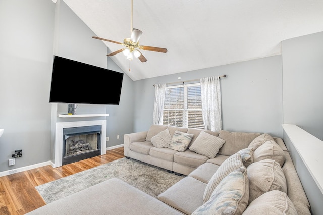 living area with high vaulted ceiling, a ceiling fan, wood finished floors, a fireplace, and baseboards