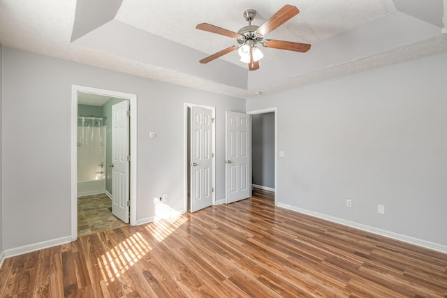 unfurnished bedroom featuring a tray ceiling, wood finished floors, baseboards, and a textured ceiling