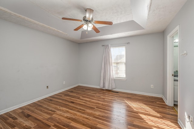 empty room with baseboards, a raised ceiling, and wood finished floors