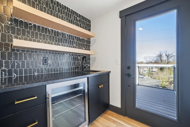 bar with light wood finished floors, a sink, wine cooler, a dry bar, and tasteful backsplash