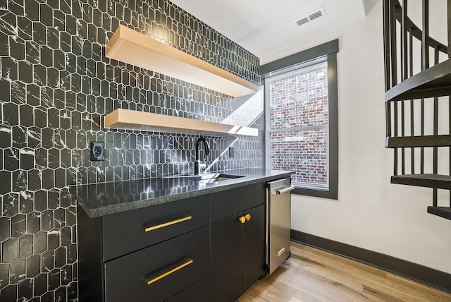 kitchen with visible vents, light wood finished floors, open shelves, stainless steel dishwasher, and dark cabinets