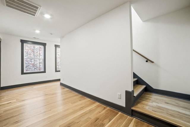 empty room featuring light wood-type flooring, visible vents, recessed lighting, baseboards, and stairs