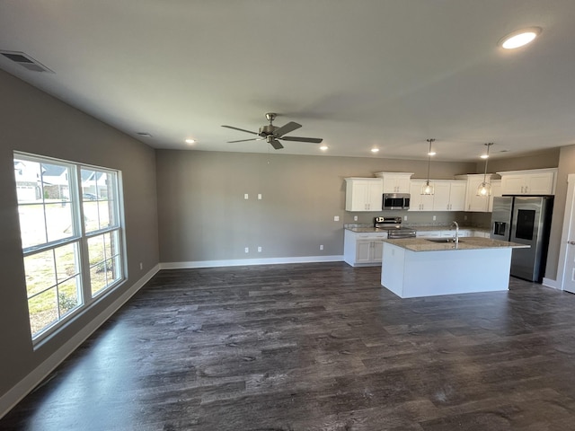 kitchen with baseboards, open floor plan, a center island with sink, stainless steel appliances, and a sink