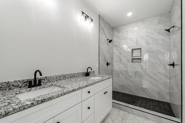 full bath featuring double vanity, marble finish floor, tiled shower, and a sink