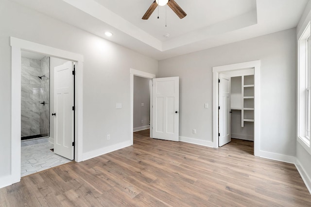 unfurnished bedroom featuring a raised ceiling, wood finished floors, baseboards, and ensuite bathroom