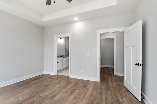 unfurnished bedroom featuring a tray ceiling, wood finished floors, baseboards, and ensuite bathroom