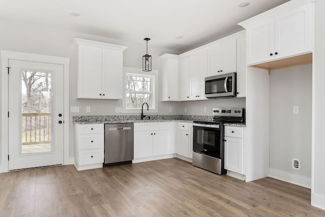 kitchen with light stone counters, appliances with stainless steel finishes, light wood-style floors, white cabinetry, and a sink