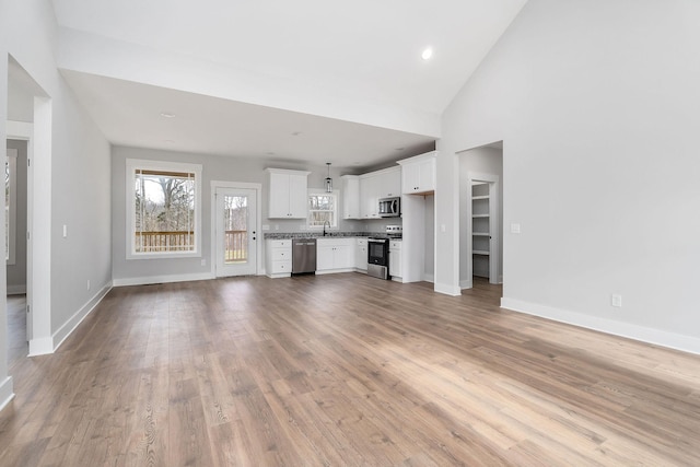 unfurnished living room featuring a sink, baseboards, high vaulted ceiling, and light wood finished floors