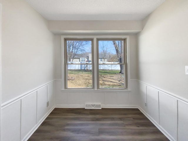 empty room with visible vents, dark wood-style flooring, and wainscoting