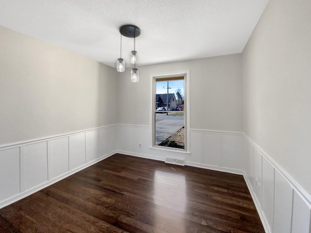 unfurnished dining area featuring visible vents, a textured ceiling, wood finished floors, and wainscoting