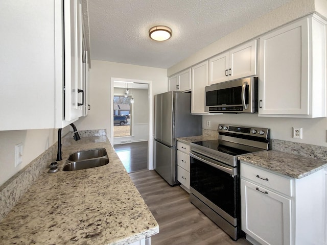 kitchen with a sink, a textured ceiling, wood finished floors, stainless steel appliances, and white cabinets