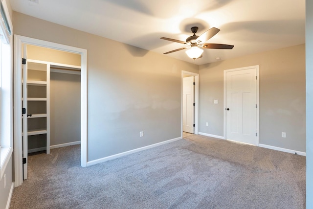 unfurnished bedroom featuring carpet, baseboards, ceiling fan, a closet, and a walk in closet