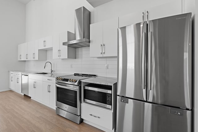 kitchen featuring light wood finished floors, a sink, stainless steel appliances, wall chimney exhaust hood, and tasteful backsplash