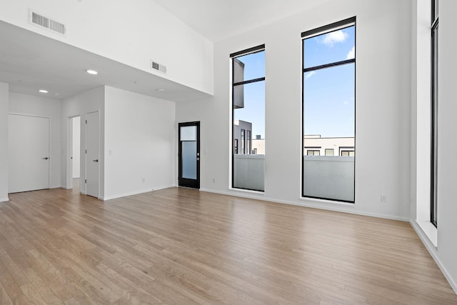 spare room featuring visible vents, baseboards, light wood-style flooring, and a towering ceiling