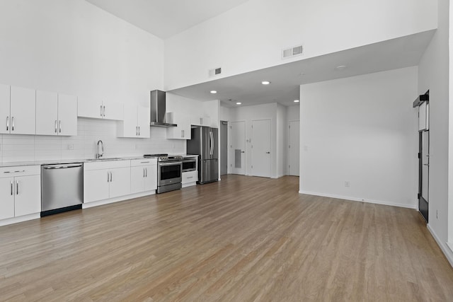 kitchen with visible vents, a sink, a towering ceiling, appliances with stainless steel finishes, and wall chimney exhaust hood