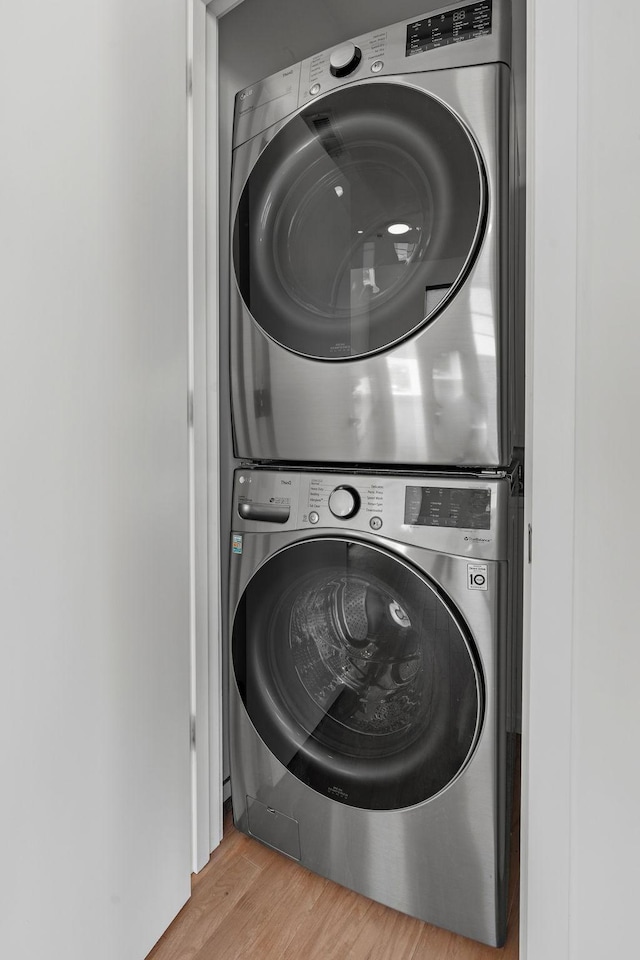 clothes washing area with laundry area, wood finished floors, and stacked washing maching and dryer