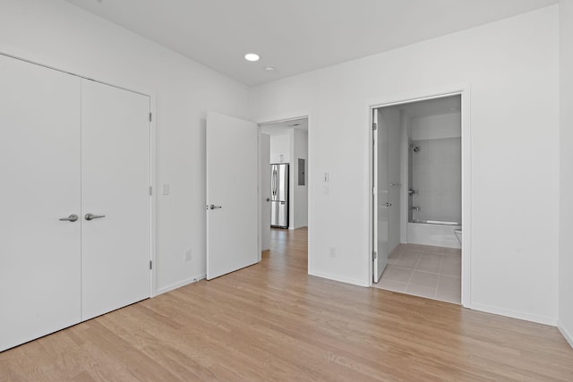 unfurnished bedroom featuring baseboards, ensuite bath, light wood-style flooring, freestanding refrigerator, and a closet