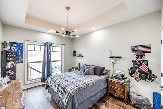 bedroom with a tray ceiling, an inviting chandelier, and dark wood finished floors