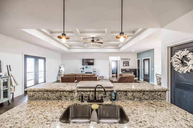 kitchen with a sink, light stone counters, coffered ceiling, dark wood-style floors, and french doors