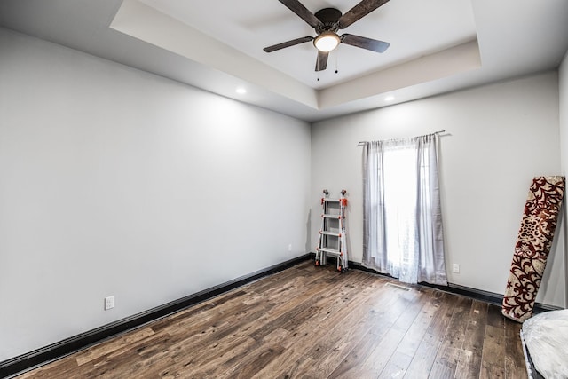 spare room with baseboards, a tray ceiling, recessed lighting, a ceiling fan, and dark wood-style flooring