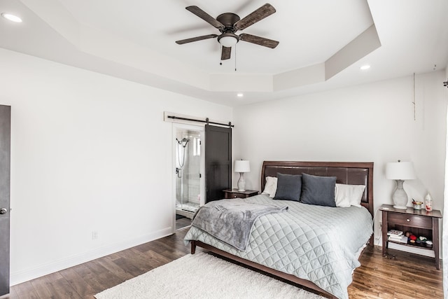 bedroom featuring a tray ceiling, a barn door, wood finished floors, and baseboards