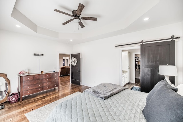 bedroom with recessed lighting, a barn door, a raised ceiling, and wood finished floors