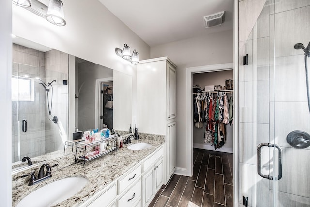 bathroom featuring visible vents, a walk in closet, wood finish floors, a stall shower, and a sink