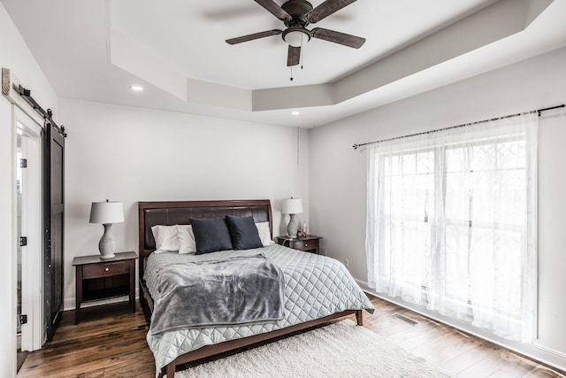 bedroom with wood finished floors, baseboards, a tray ceiling, recessed lighting, and a barn door