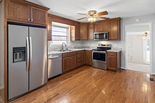 kitchen featuring light wood-style flooring, stainless steel appliances, a ceiling fan, and a sink
