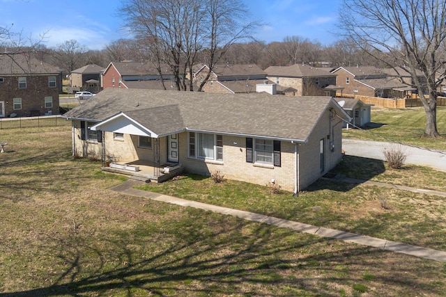 view of front facade with fence, a residential view, a front yard, a shingled roof, and brick siding